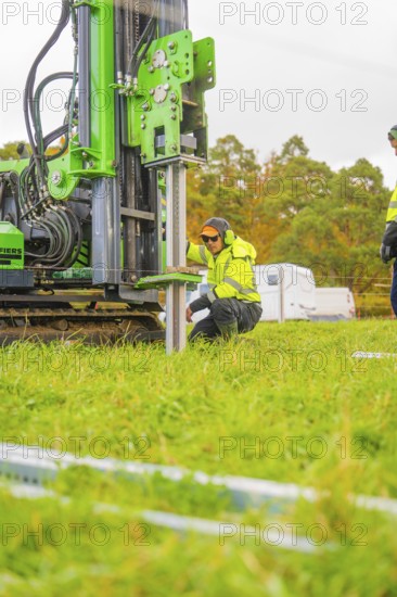 A worker kneels next to a drilling rig in a meadow and adjusts the machine, Energiewende, construction of PV open space, Baden-Württemberg, Germany