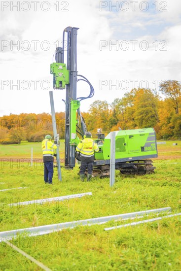 Two workers set up posts in a meadow with a drilling rig, Energiewende, construction of PV open space, Baden-Württemberg, Germany