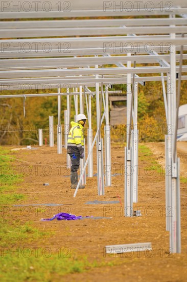 Craftsman in safety clothing working on the construction of solar panels in an open field, Energiewende, construction of PV open space, Baden-Württemberg, Germany