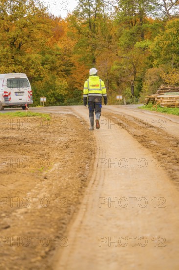 A worker in safety clothing walks on a dirt road through an autumn landscape, Energiewende, construction of PV open space, Baden-Württemberg, Germany