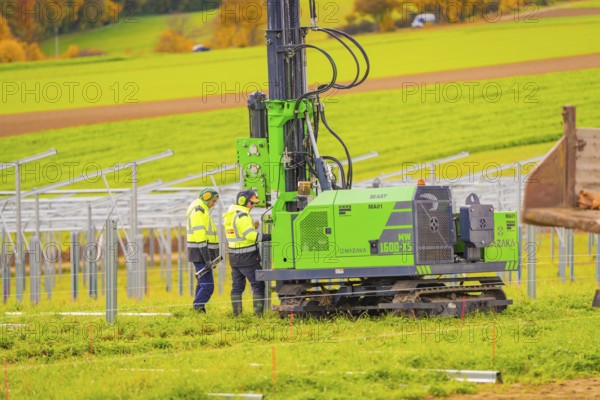 Workers in safety vests monitor the installation of metal structures in an open field, Energiewende, construction of PV open space, Baden-Württemberg, Germany