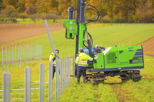Green machine and worker installing metal poles in the field on a sunny autumn day, Energiewende, construction of PV open space, Baden-Württemberg, Germany