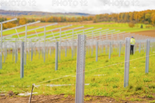 Metal poles along a field under cloudy sky with autumn landscape in the background, Energiewende, construction of PV open space, Baden-Württemberg, Germany