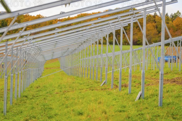 A long metal framework runs on a green field in autumn, surrounded by trees, energy transition, construction of PV open space, Baden-Württemberg, Germany