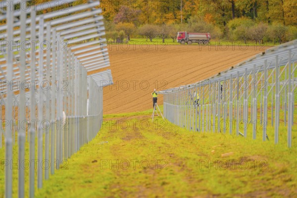 A farm worker on a ladder between metal structures with a tractor in the background in an autumn landscape, energy transition, construction of PV open space, Baden-Württemberg, Germany