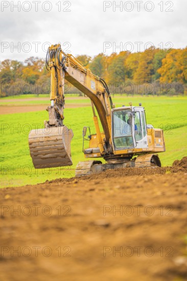 Excavator lifts soil in a green landscape with autumn trees, energy revolution, construction of PV open space, Baden-Württemberg, Germany