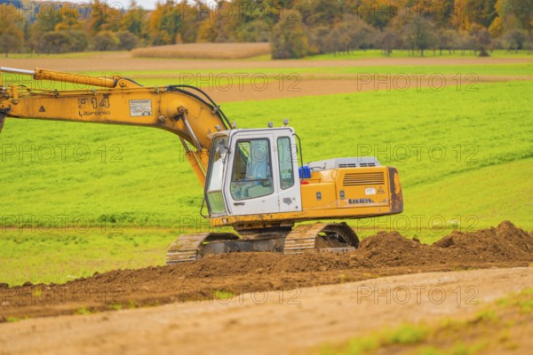 Large yellow excavator operating on an open, green area, energy revolution, construction of PV open space, Baden-Württemberg, Germany