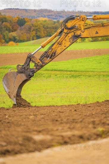 Close-up of an excavator bucket moving earth surrounded by green fields, energy transition, construction of PV open space, Baden-Württemberg, Germany