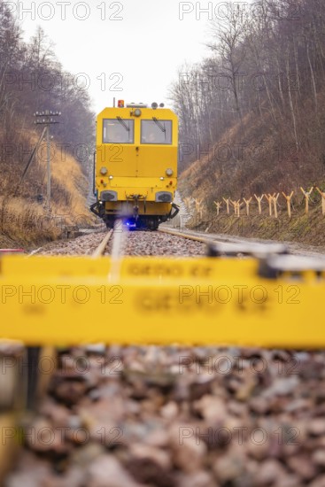 A yellow vehicle travels on rails with a Gedo CE device in the foreground, tamping machine on Hermann, Hesse, Bahn, Althengstett, Calw district, Germany
