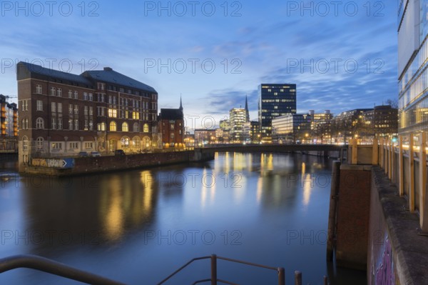 View from Oberbaum Bridge of the Zollkanal and Teerhof at blue hour with reflections in the water and light cloudiness in the background, Speicherstadt, Hamburg, Germany