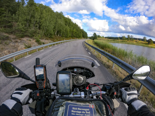 A motorcyclist's view of an empty country road surrounded by green trees and a lake under a blue sky, navigation system, GPS, tank bag with map, Sparreholm, Södermanslän, Sweden