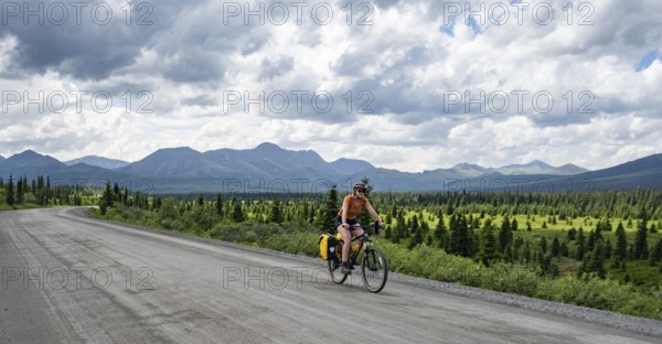 Young woman riding a bicycle on a dirt road through the tundra, mountainous landscape, Denali Park Road, Denali National Park and Preserve, Alaska, USA