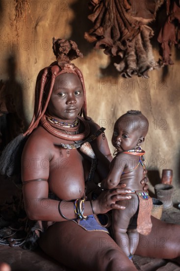 Himba woman sitting with baby in traditional hut, Himba village, Kaokoveld, Kunene, Namibia