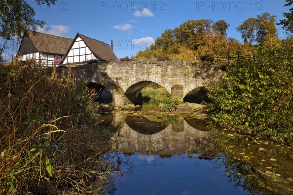 The river Hönne with the old Hönnetalbrücke in autumn with half-timbered house in Volkringhausen, Balve, Sauerland, North Rhine-Westphalia, Germany