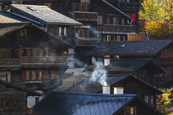 Smoke rises over the roofs of old wooden houses in Vissoie, Val d'Anniviers, Valais Alps, Canton of Valais, Switzerland