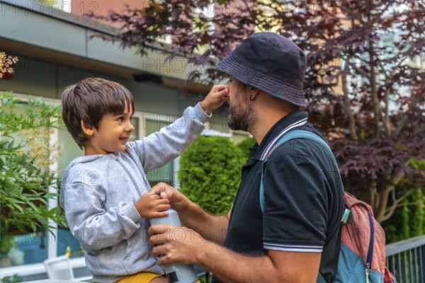 Playful preschool child touching his father's nose while holding a water bottle in a residential area of vancouver, british columbia, showing a tender moment of family bonding
