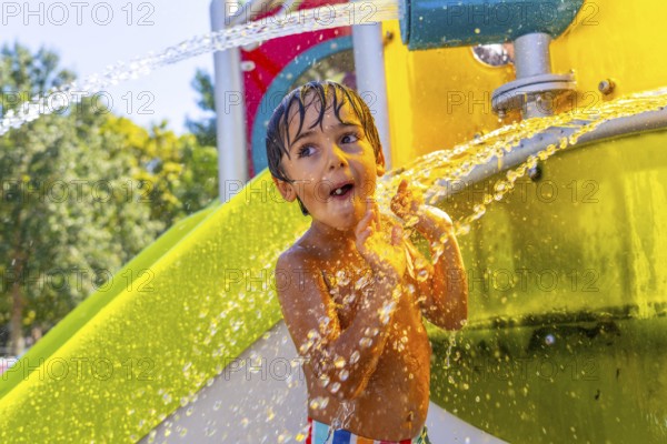 Young boy is having fun playing under refreshing water jets at a colorful water park in kamloops, british columbia, experiencing the joy of summer