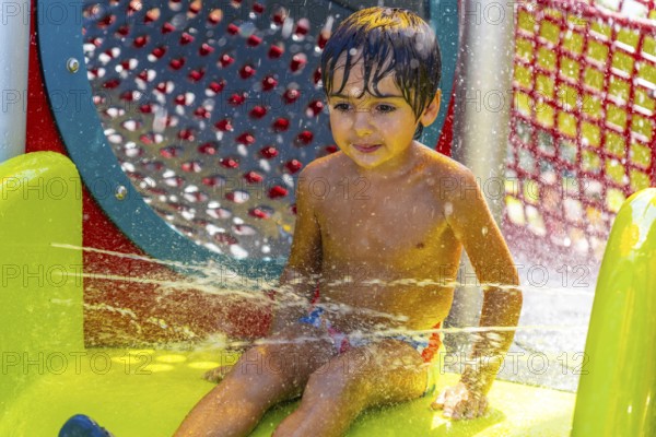 Young boy is having fun playing and splashing in the water jets at a colorful splash park in kamloops, british columbia, enjoying a refreshing summer day outdoors