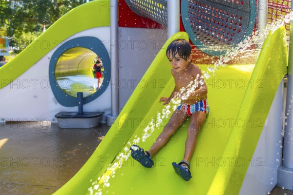 Happy child enjoying a sunny summer day, sliding down a bright green water slide at a splash park, getting sprayed with refreshing water in kamloops, british columbia, canada