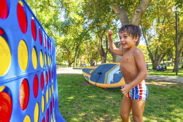 Happy child celebrating winning a game of giant four in a row in a park in kamloops, british columbia, with inflatable stand up paddleboard in the background on a sunny summer day