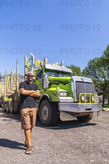 Truck driver standing with arms crossed in front of his logging truck on a sunny day in kamloops, british columbia, canada, showcasing pride in his profession and the impressive machinery