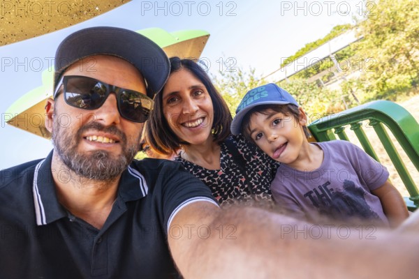 Happy family consisting of a father, mother, and son taking a selfie while enjoying a ride on a miniature train in a park in kamloops, british columbia, canada, during a sunny summer day