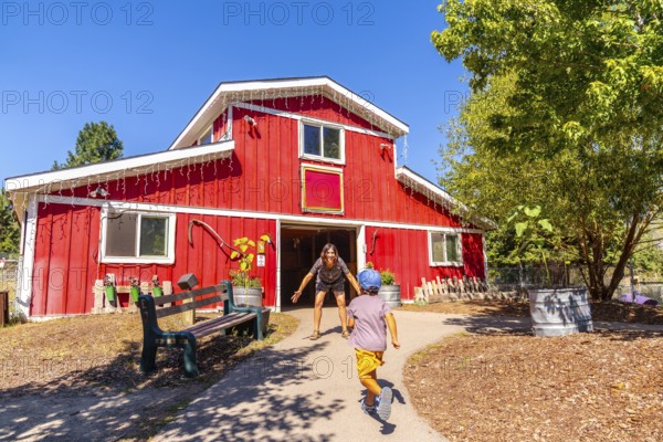 Child runs towards their mother who is waiting with open arms in front of a bright red barn at the bc wildlife park in kamloops, british columbia on a sunny day