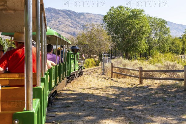 Tourists enjoying a delightful ride on a miniature train, taking in the stunning landscapes of kamloops, british columbia, under the warm sun on a beautiful summer day