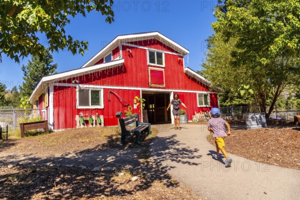 Mother with open arms welcoming her son, joyfully running toward her at the entrance of a large red barn on a sunny summer day, surrounded by the beauty of nature on the farm