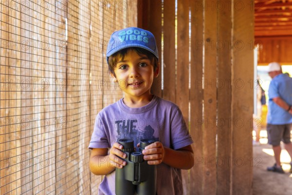 Curious child holding binoculars, exploring the wonders of nature at the british columbia wildlife park in kamloops, wearing a good vibes cap, ready for an adventurous day of discovery and learning