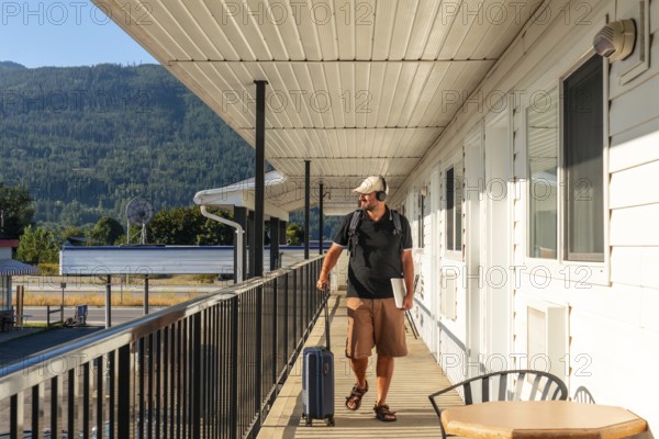 Digital nomad walking along a motel balcony, surrounded by luggage and a laptop, soaking in the breathtaking mountain view while enjoying a productive workation