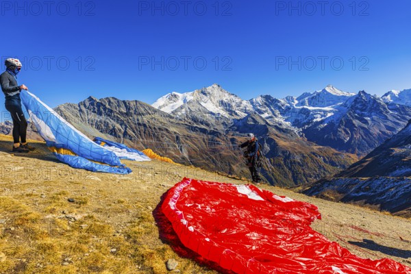 Paragliders are preparing for their start, with the snow-capped peaks of the Valais Alps, Val d'Anniviers, Canton of Valais, Switzerland