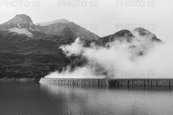 Fog rises over the dam of the Lac de Moiry reservoir, black and white photo, Val d'Anniviers, Valais Alps, Canton of Valais, Switzerland