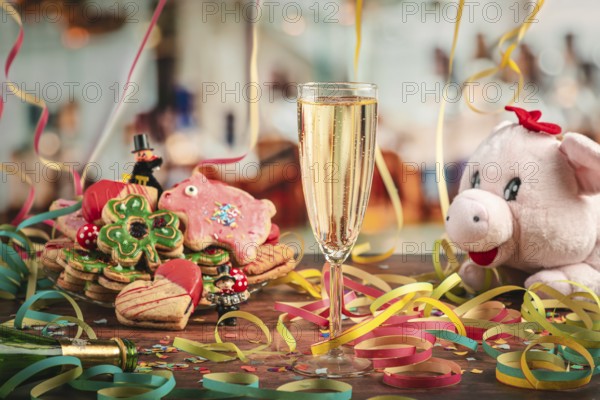 Filled champagne glass surrounded by New Year cookies, streamers and plush pig