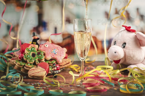 Pour sparkling wine into glass surrounded by New Year cookies, streamers and a plush pig