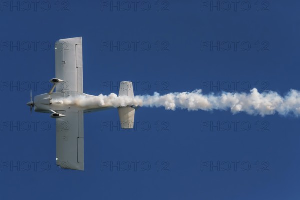 Stunt aerobatic plane performing stunts in blue sky with smoke trail. Concept of speed, difficulty, precision, risk, challenge