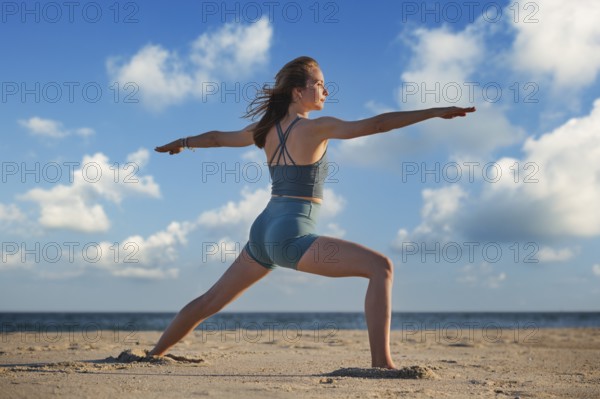 A woman practices Warrior 2 Virabhadrasana 2 pose on the beach during sunset, embodying strength and peace in her yoga practice