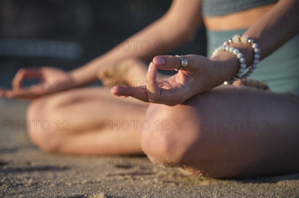 Woman meditates in Padmasana on the beach, using Chin mudra hand gesture in a tranquil setting during sunset