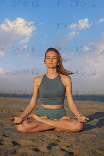 A woman performs Ashtanga Vinyasa yoga in Padmasana with Chin mudra on the beach, meditating peacefully as the sun sets