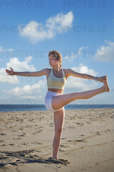 Woman yoga practice at the beach in Utthita Hasta Padangusthasana Extended Hand-to-Big-Toe Pose