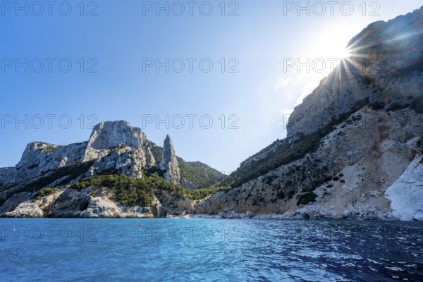 Light blue clear sea on a dream beach on Cala Goloritzé, picturesque rocky coast with sun stars, cliffs with rock peak L'Aguglia, Golfo di Orosei, Baunei, Sardinia, Italy