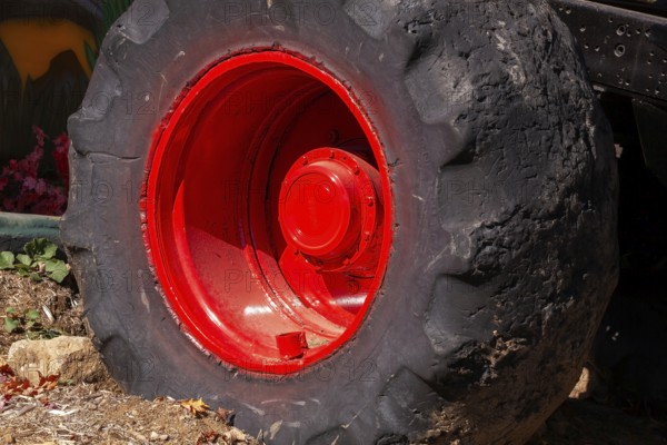 Close-up and rear side view of large heavy duty black rubber tire mounted on red rim on monster truck vehicle, Quebec, Canada