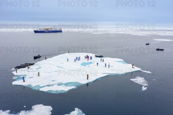 Aerial view over ecotourists from Iceland Pro Cruises walking on ice floe drifting in the Arctic Ocean in summer at Svalbard / Spitsbergen, Norway