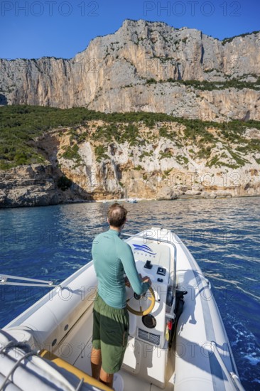 Young man rides a motorboat along the picturesque rocky coast, cliffs and blue sea, Golfo di Orosei, Baunei, Sardinia, Italy