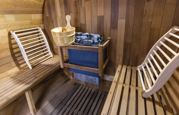 Steam and hot stone wooden cedar compact sauna interior with heating stone electrical device, hot water bucket and benches