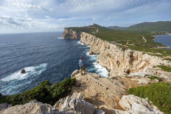 Tourist enjoying the view of steep cliffs by the sea, coastal landscape, cliffs on the Capo Caccia headland, Alghero, Sardinia, Italy