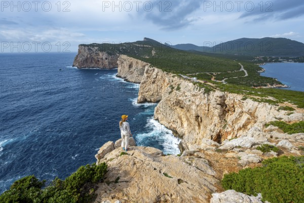 Tourist enjoying the view of steep cliffs by the sea, coastal landscape, cliffs on the Capo Caccia headland, Alghero, Sardinia, Italy