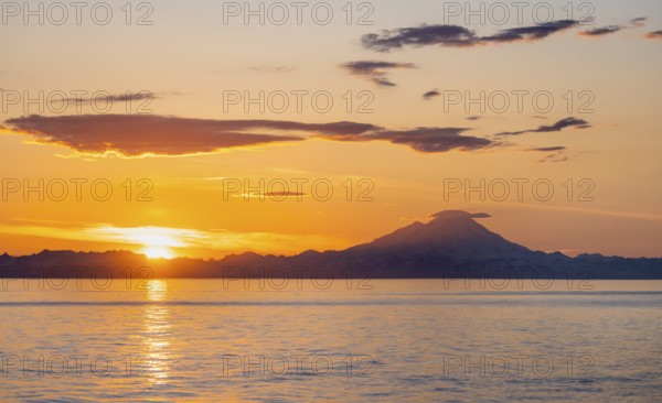 View of Cook Inlet on white mountain peaks of Mount Redoubt at sunset, picturesque golden light of the midnight sun, mountains of the Aleutian Range, Anchor Point, Anchor River State Recreation Area, Alaska, USA