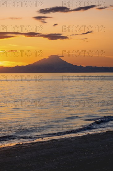 View of Cook Inlet on white mountain peaks of Mount Redoubt at sunset, picturesque golden light of the midnight sun, mountains of the Aleutian Range, Anchor Point, Anchor River State Recreation Area, Alaska, USA