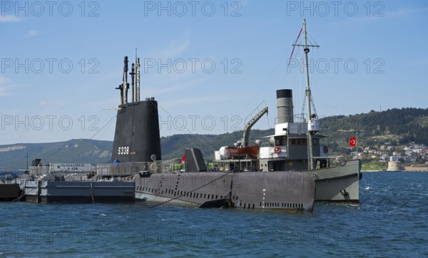 Submarine and ship in harbor overlooking a distant city and hills, TCG Uluçalireis S-338, War Museum, in the background Kilitbahir, Çanakkale, Canakkale, Marmara region, Turkey